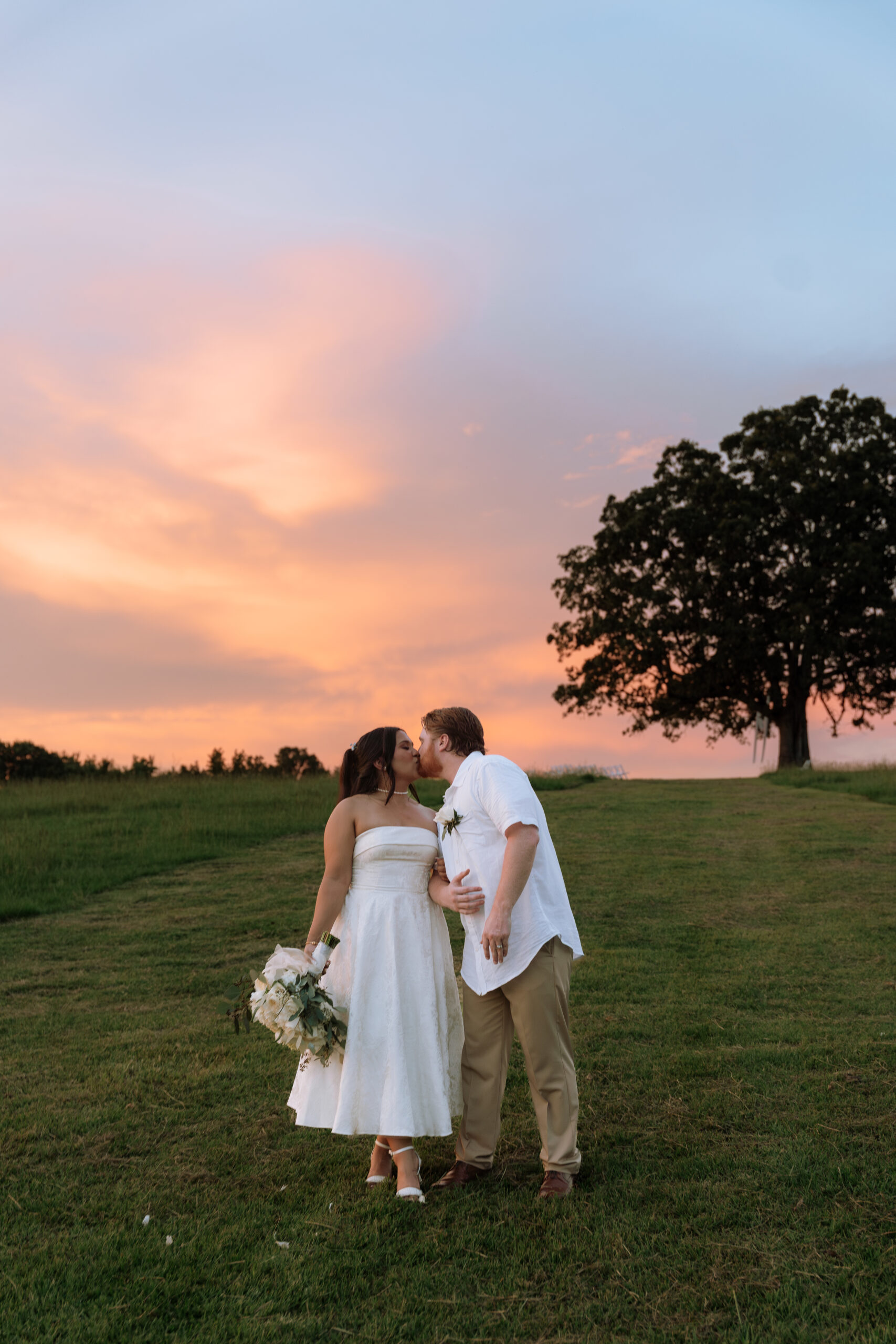 A couple kissing under an oak tree during sunset.
